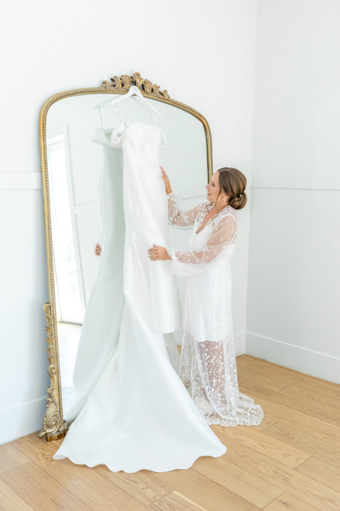 bride looking at her wedding gown in front of big mirror