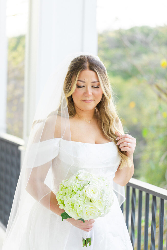 Bride smiling down at her bouquet on the Kendall Point wedding venue porch